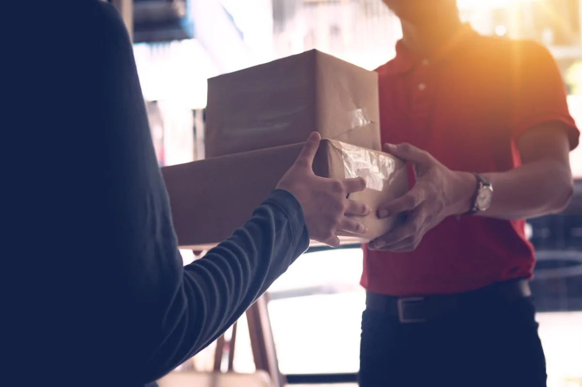 Un coursier remet un colis en main propre à un client