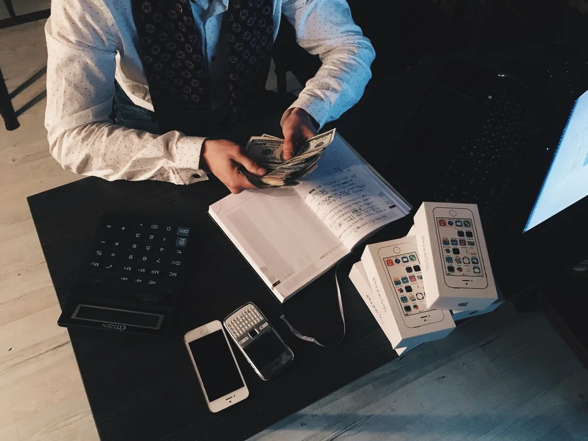 Un commerçant compte des billets à son bureau, carnet et téléphone à portée de main
