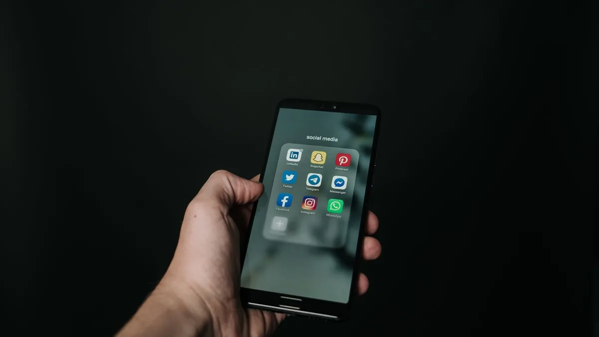 Une main tient un smartphone affichant les icônes de WhatsApp, Facebook et Instagram